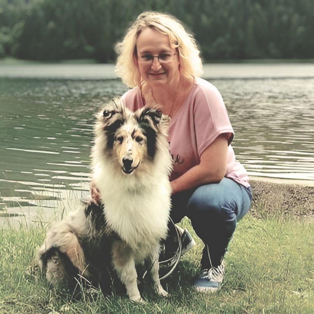 Birgit, die Gründerin von Mein Collie, sitzt lächelnd mit ihrem Langhaarcollie am Ufer eines Sees